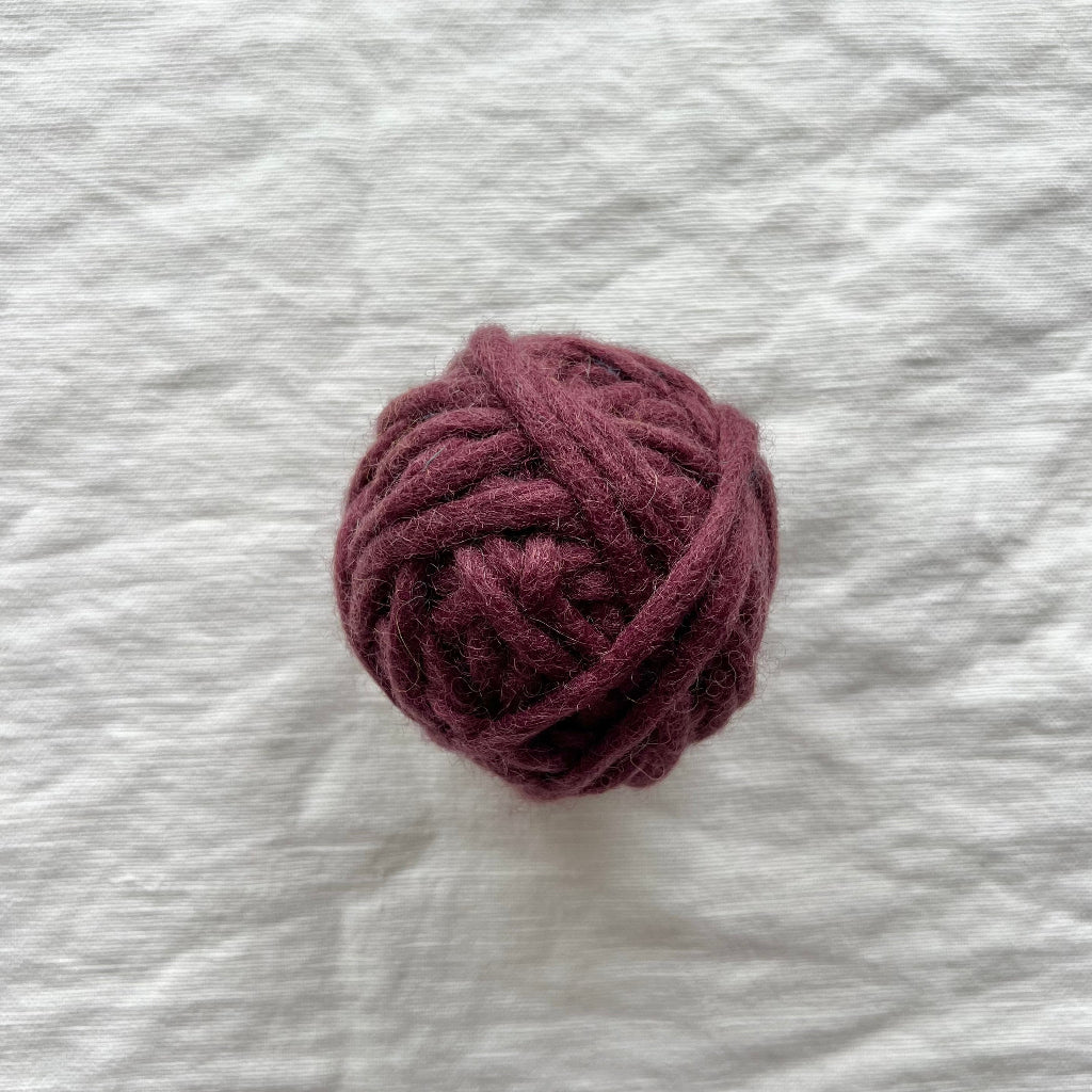 Ball of dark purple yarn on a textured white fabric background