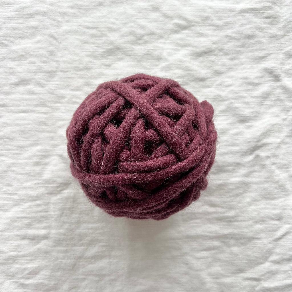 Ball of dark purple yarn on a textured white background