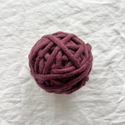 Ball of dark purple yarn on a textured white background