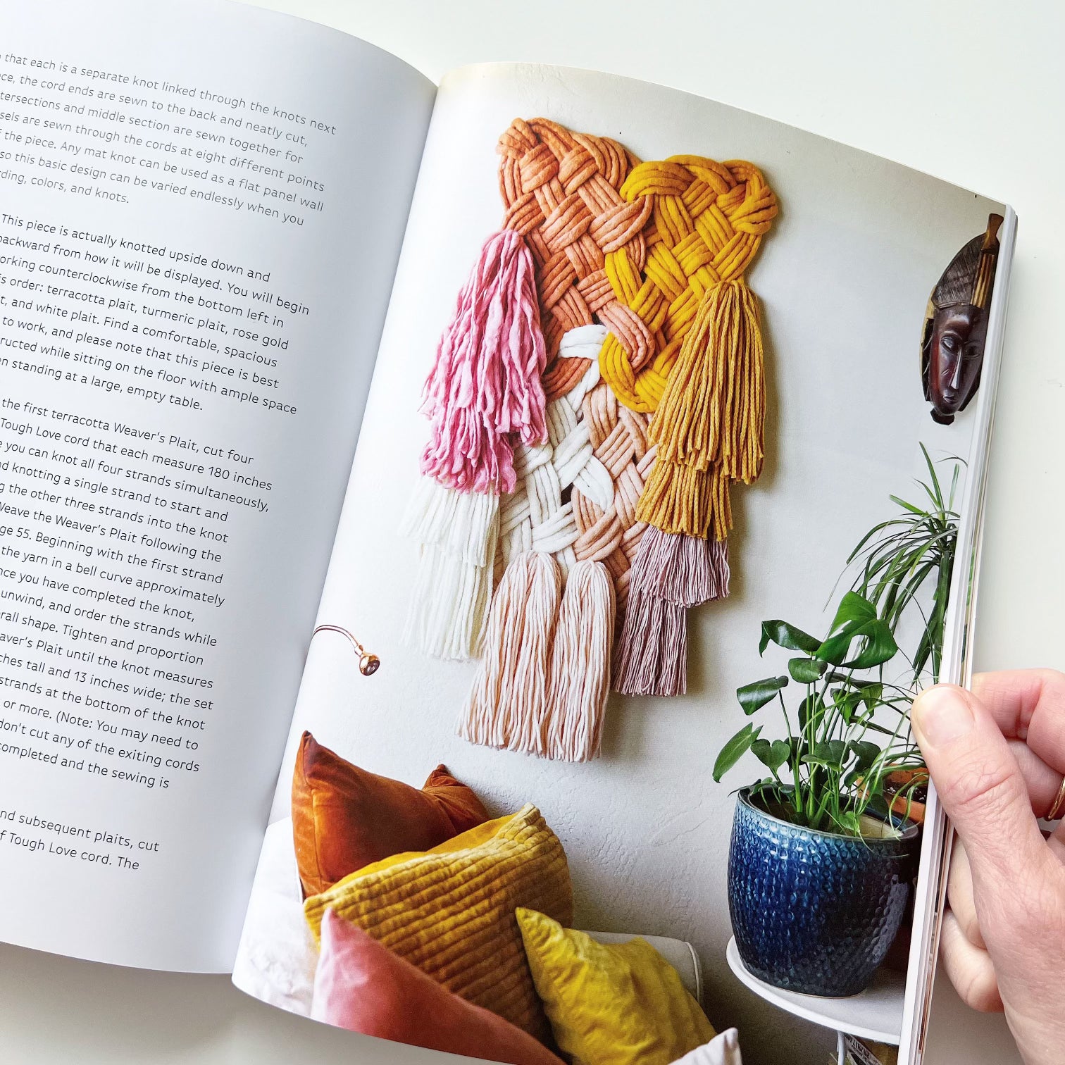 Open book with colorful woven wall art and indoor plants on a table