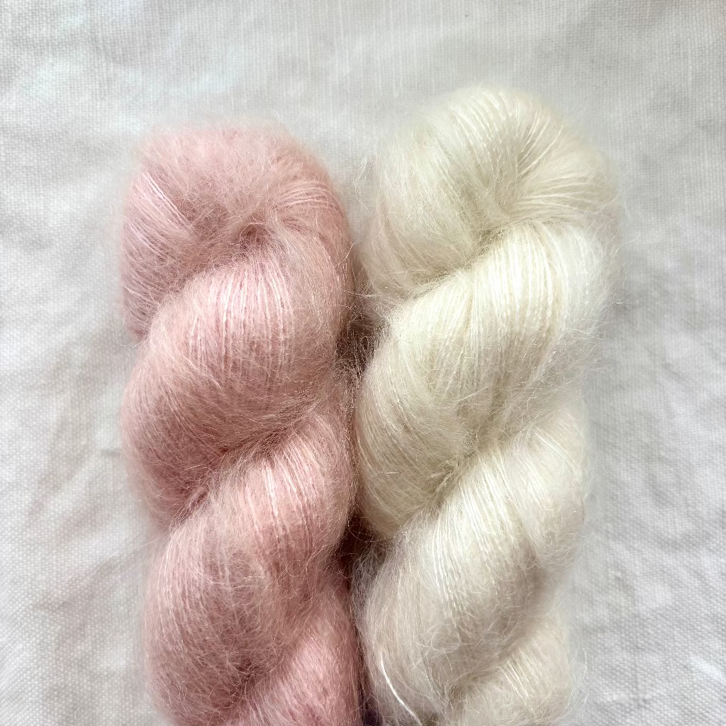Two skeins of soft pink and white yarn on a textured light gray background
