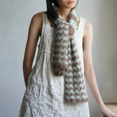 Person wearing a white dress and a brown and white checkered scarf against a neutral background