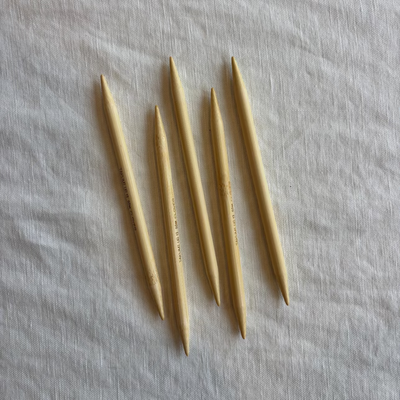 Set of five wooden knitting needles on a light fabric background