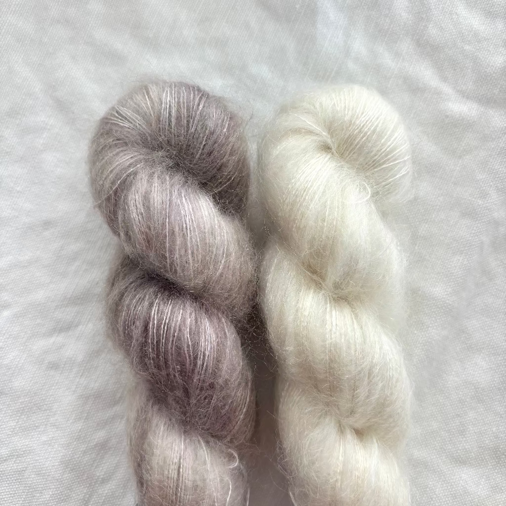 Two skeins of yarn, one white and one grayish-beige, on a textured white background.